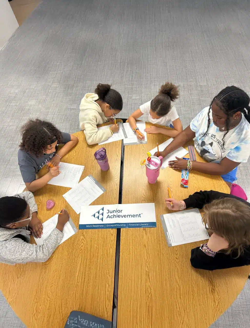 Students participating in a Junior Achievement classroom activity around a table